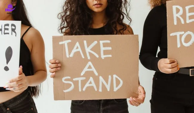 Womens stand with board written "Take a Stand" & Overcoming Challenges and Staying Informed